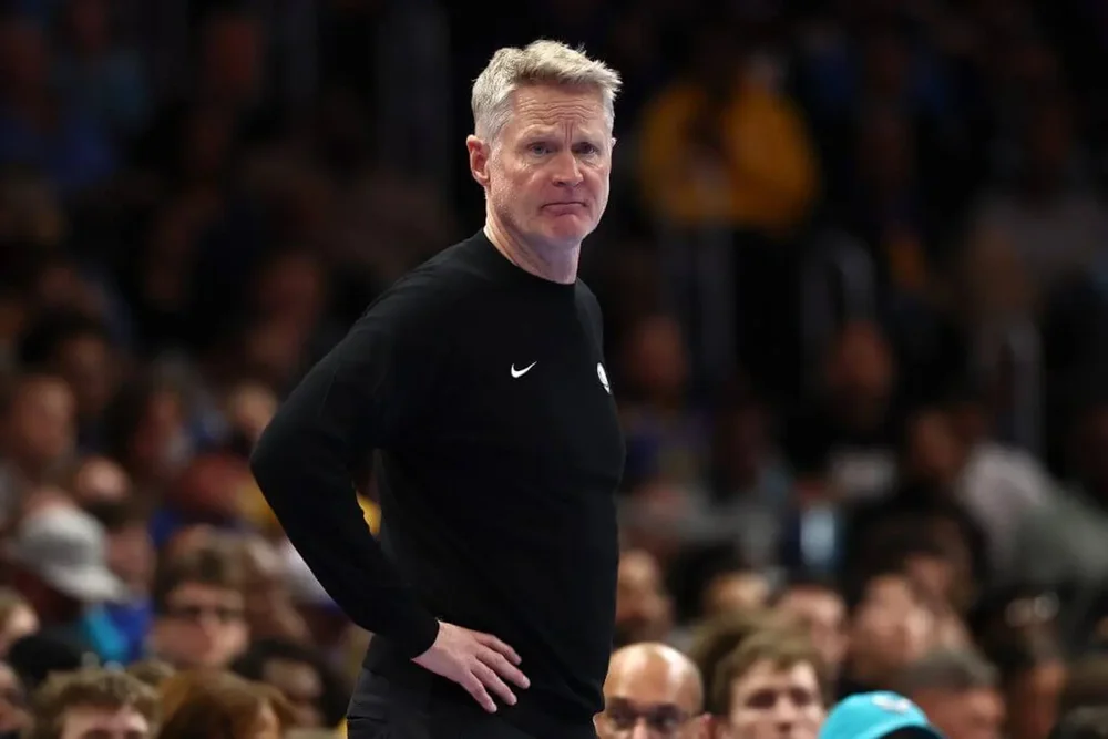 Golden State Warriors coach Steve Kerr rests his hands on his hips while watching a game from the sideline.
